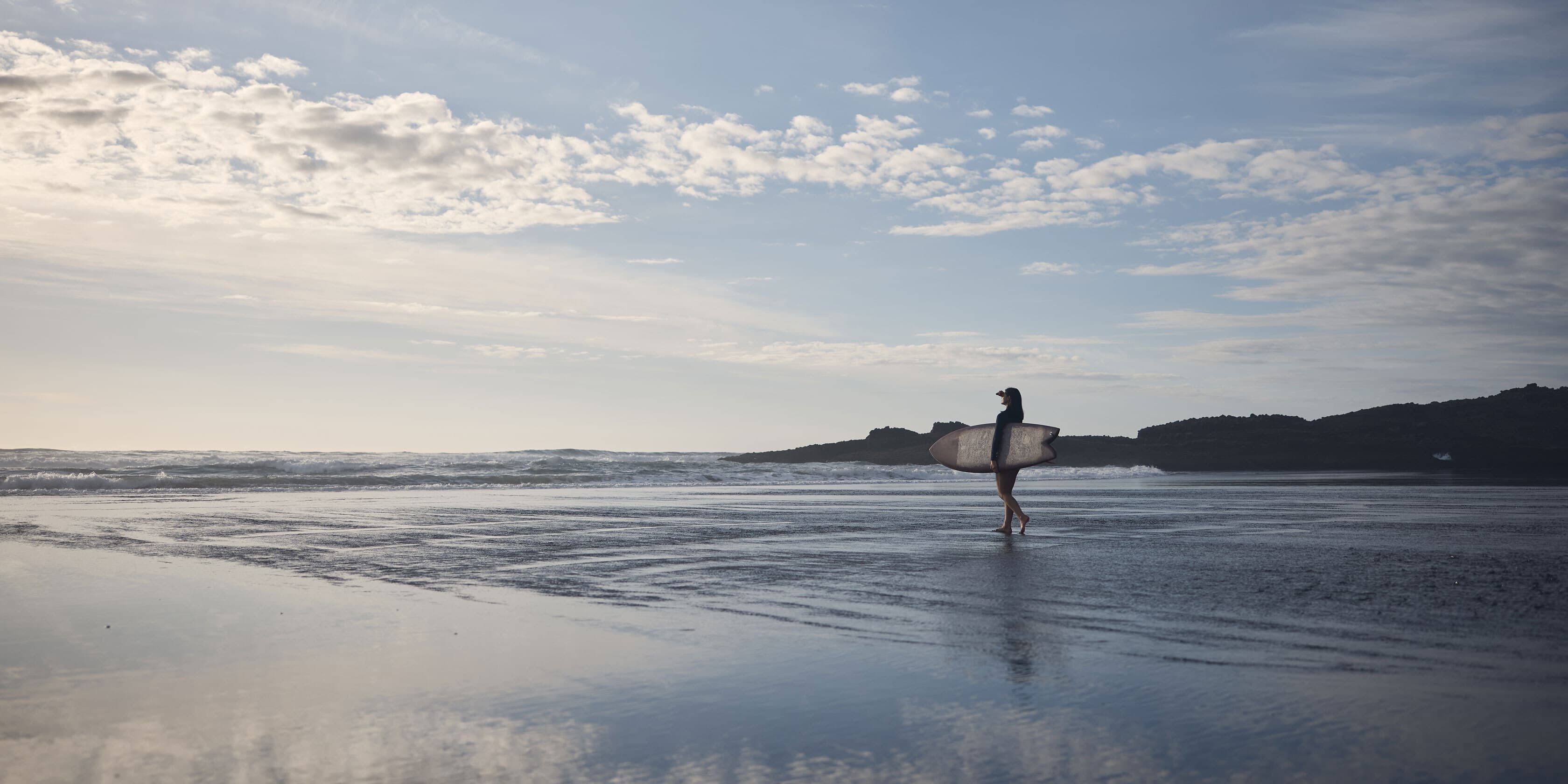 Lady walking into water with a surfboard at the beach