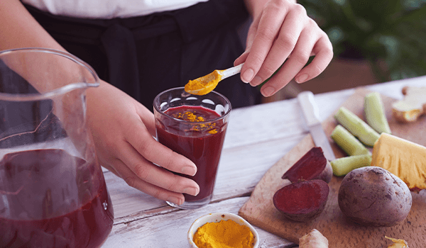 Someone adding a teaspoon of turmeric to beetroot juice