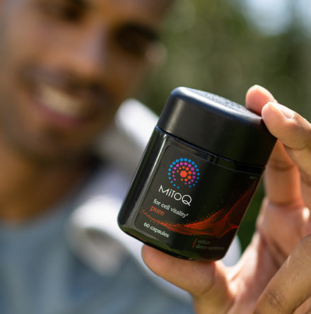 Man in the background blurry holding MitoQ Pure in the foreground in frame